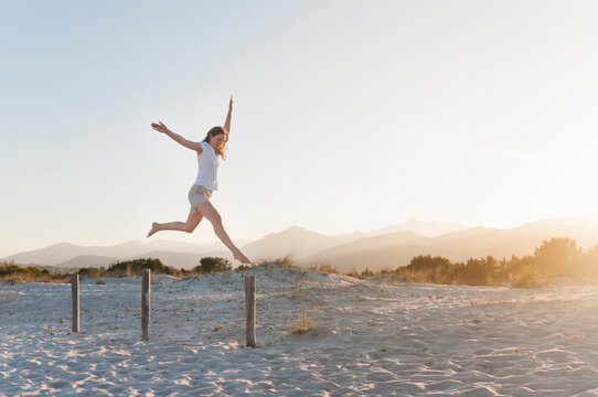 Happy woman jumping in the air on the beach, Sardinia, Italy