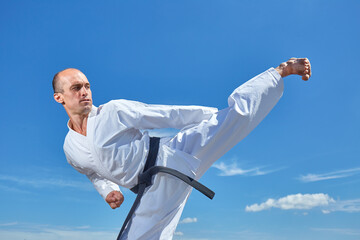 An athlete performs a kick to the side against a blue sky