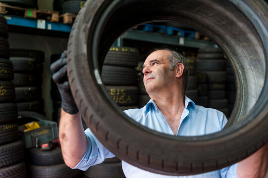Senior male entrepreneur holding tire while working at store
