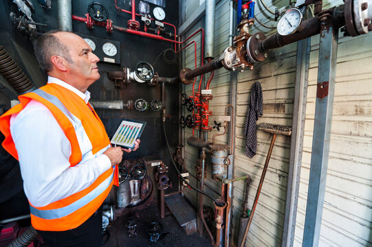 Senior man with tablet wearing safety vest examining a machine