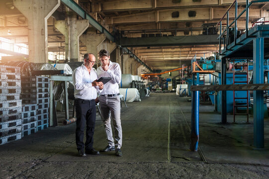 Two businessmen having a meeting looking at tablet in a factory hall