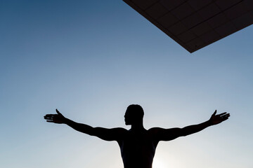 Silhouette of man stretching out arms, against clear sky