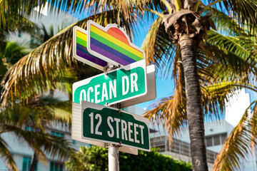 Road signs with rainbow flags against palm trees at ocean drive