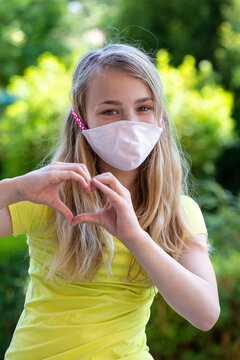 Girl Wearing Protective Mask And Forming A Heart With Her Hands Outdoors