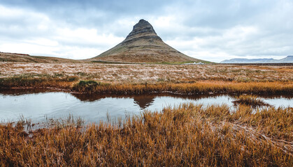 Fototapeta premium Scenic image of Iceland. The Kirkjufell volcano the coast of Snaefellsnes peninsula with overcast sky at Autumn time. Majestic Kirkjufell (Church mountain) the most famous icelandic landmark. Postcard