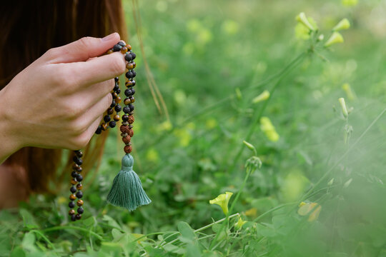 Close-up of mid adult woman holding prayer beads meditating over grassy land