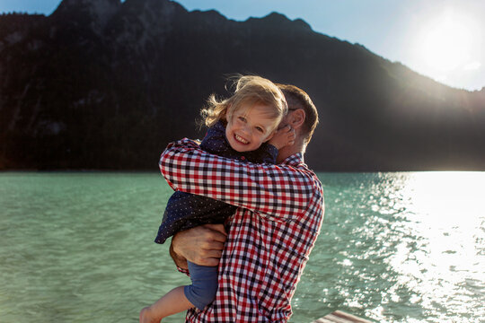 Father carrying cheerful daughter by lake Achen