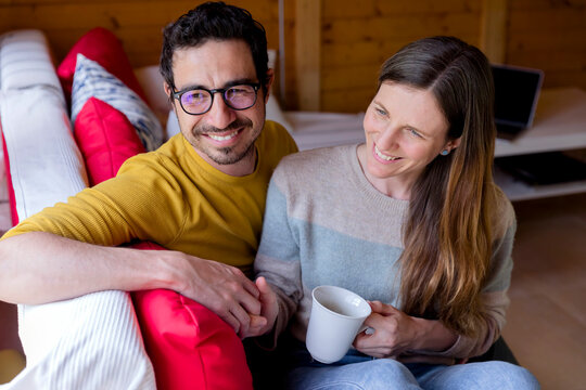 Smiling couple holding hands while relaxing on sofa in log cabin