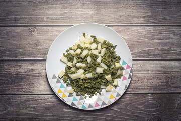 boiled potato with beans cut on dices served on a white plate on a wooden table