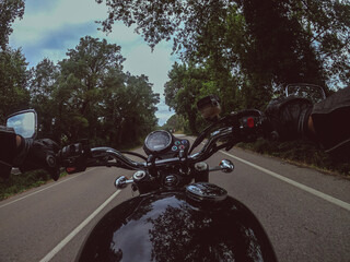 Riding a black old motorbike with black fuel tank on a cloudy landscape on an asphalt road