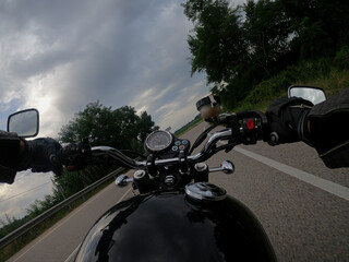 Riding a black old motorbike with black fuel tank on a cloudy landscape on an asphalt road