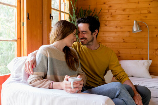 Smiling couple romancing while sitting on sofa in log cabin - Powered by Adobe