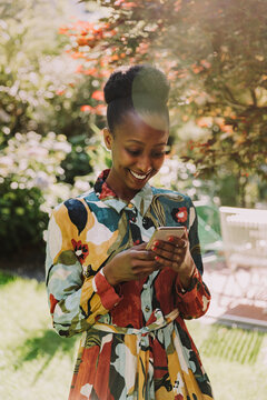 Smiling woman in fashionable dress using smartphone in garden