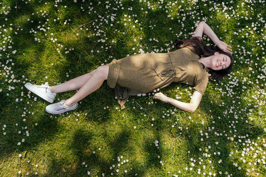 Woman enjoying her free time while lying on grass with daisies