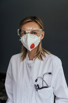 Portrait of doctor wearing FFP3 mask and safety glasses against grey background