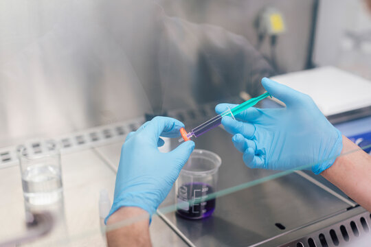 Hands of male technician holding syringe with chemical over beaker in lab