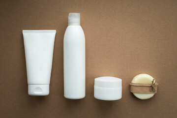 MOCKUP contrasting plastic to zero waste: a white tube of cream, a white bottle of shampoo and a white jar of face cream along with a bar of dry shampoo soap on a craft background