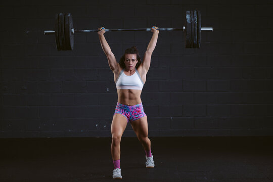 Young woman practicing barbell squat at gym
