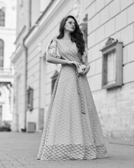 Elegant woman in blue ball gown. Brunette female fashion model standing at city street and posing. Lady with makeup and wavy hair. Caucasian girl outdoor full length fashion portrait