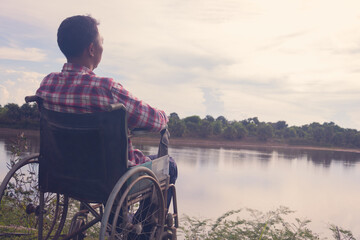 Young disabled man with river background.He is sitting on wheelchair and looking into river.