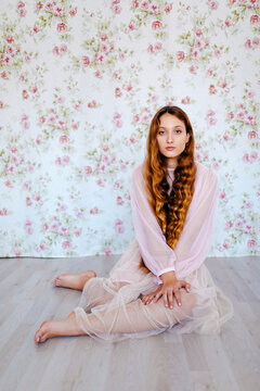 Portrait of confident young woman with long brown hair sitting against floral wallpaper
