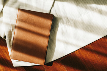 Brown book on top of white cloth on the floor. Sunlight and shadows can be seen.
