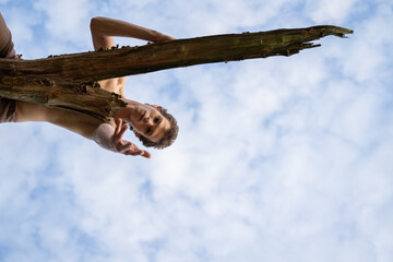 Low angle portrait of man showing hand while lying on log against cloudy sky in forest