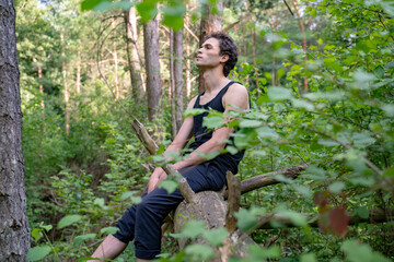 Naklejka na ściany i meble Side view of thoughtful man looking away while sitting on log against trees in forest