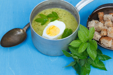 green summer soup from aegopodium, a wild herb with useful properties in a bucket with a boiled egg and a bowl of crackers, close-up