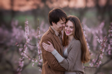 Happy couple in love hug on the background of blooming sunset gardens in spring. Romantic date for two outside the city. Evening picnic, surprise. Wedding anniversary. The lovers laugh. Close up 