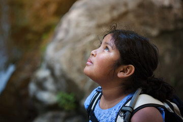 Young girl with hiking backpack looks up towards a difficult hiking trail ahead of her.