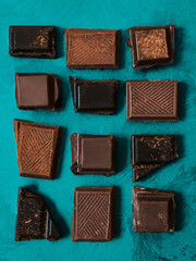 Different broken chocolate pieces Top view photo Crushed chocolate bars are lying in a rows on textured turquoise background