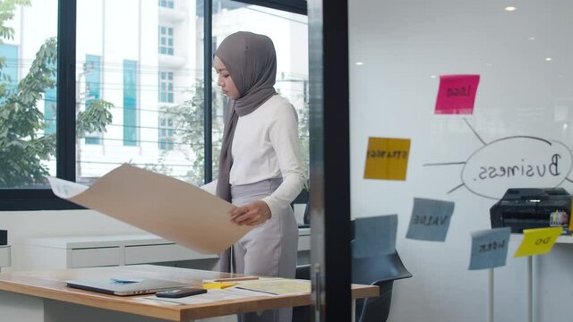 Asia muslim lady drawing work plan think information reminder on paper in new normal office. Working from home, remotely work, self isolation, social distancing, quarantine for coronavirus prevention.