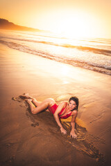 Young caucassian girl with a red bikini layed down in the beach next to the sea.