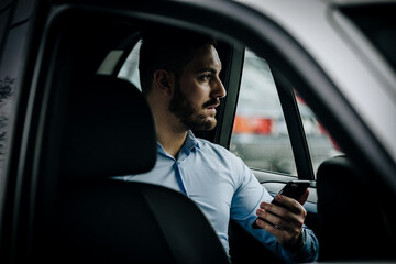 Handsome and formal looking man using his phone in the backseat of a car