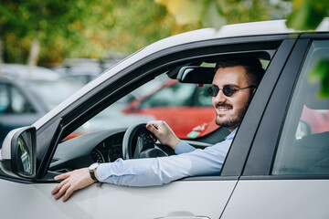 Handsome man driving a white luxury car wearing sunglasses smiling