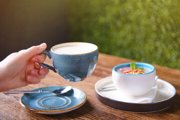 Woman hand holding a blue cup of latte coffee. Fruit dessert and milk drink in a summer cafe, close up