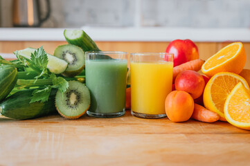 Orange juice and green juice with fresh and raw fruit in the background