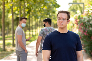 2 people with protective masks walking in the park are surprised and point to a person without a mask walking in the park and feel uncomfortable