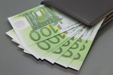 One hundred euro bills, various banknotes inside a wallet, close-up on dark background. Cash money