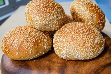 Composition in daylight, in a home interior. Ruddy homemade sesame seed buns on a flat dark wood plate