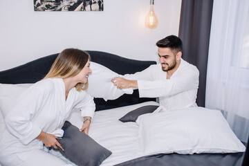 couple having a pillow fight on their bed in bathrobes 