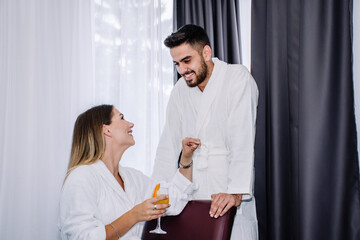 couple in love looking at each other  while the woman is holding orange juice, both wearing bathrobes