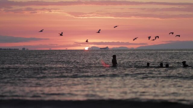 Kids playing in ocean at sunset with birds flying in Central America
