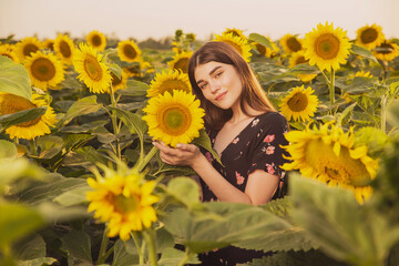 A Women in a short summer sundress poses against the background of a sunflower field, expressive and emotional summer portraits in the rays of the sunset on a background of flowers