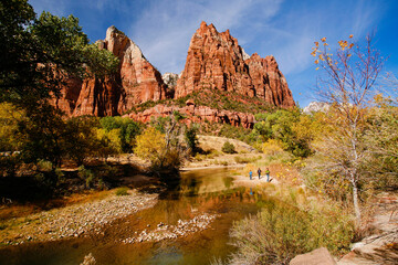 Three people walking along the Virgin River in Zion National Park during the fal season.  Trees showing fall colors line the river.