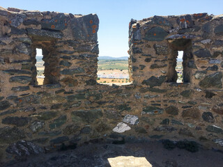 View behind ancient stone battlements and loopholes with countryside and distant horizon under blue sky in natural light. Full frame of rough stone texture and gentle nature with copy space.