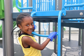 Girl smiling and playing on playground wearing  blue latex gloves on summer day