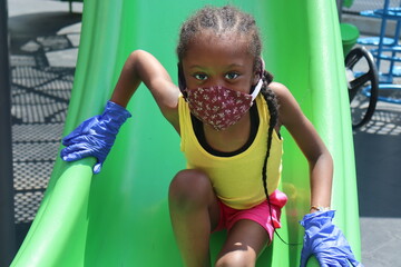 Girl on playground slide wearing face mask and gloves