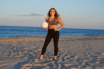 Fototapeta na wymiar Stunning young blonde woman with volleyball on beach at sunset